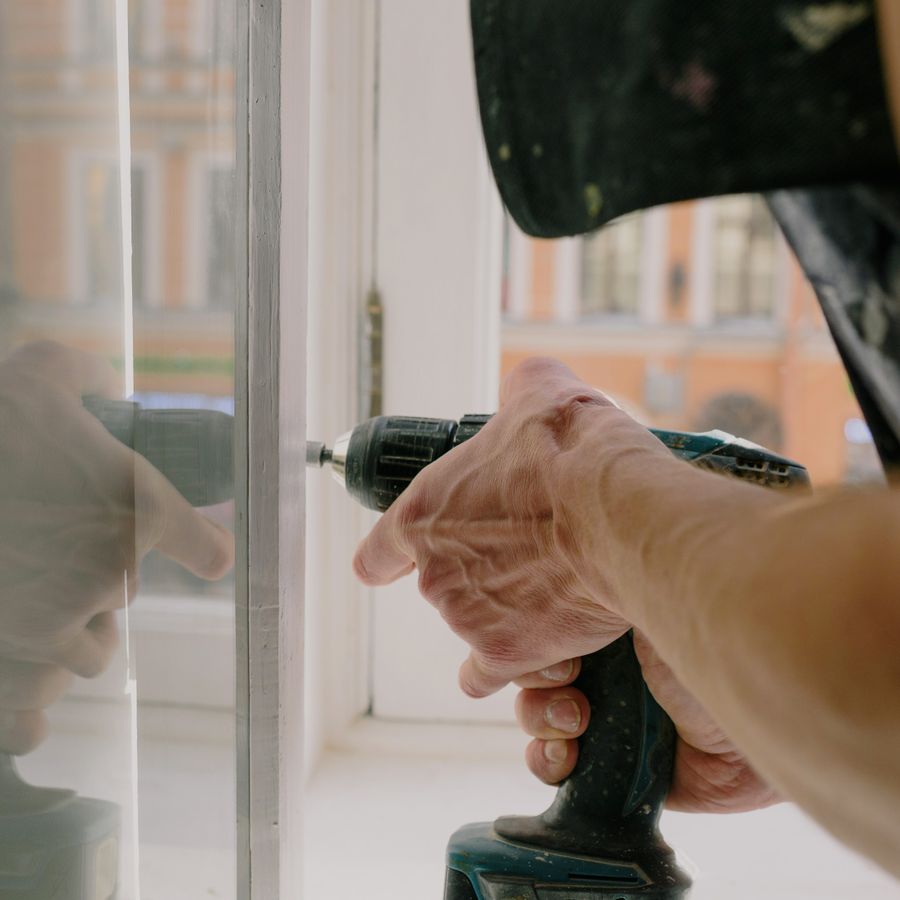 Hände justieren einen Fensterbeschlag mit dem Akkuschrauber