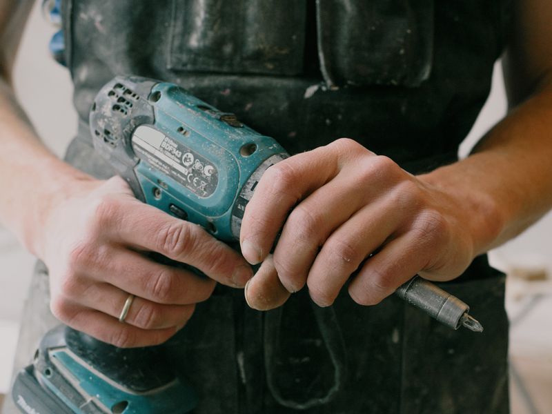 Hände eines Handwerkers mit Akkuschrauber und Werkzeugschürze